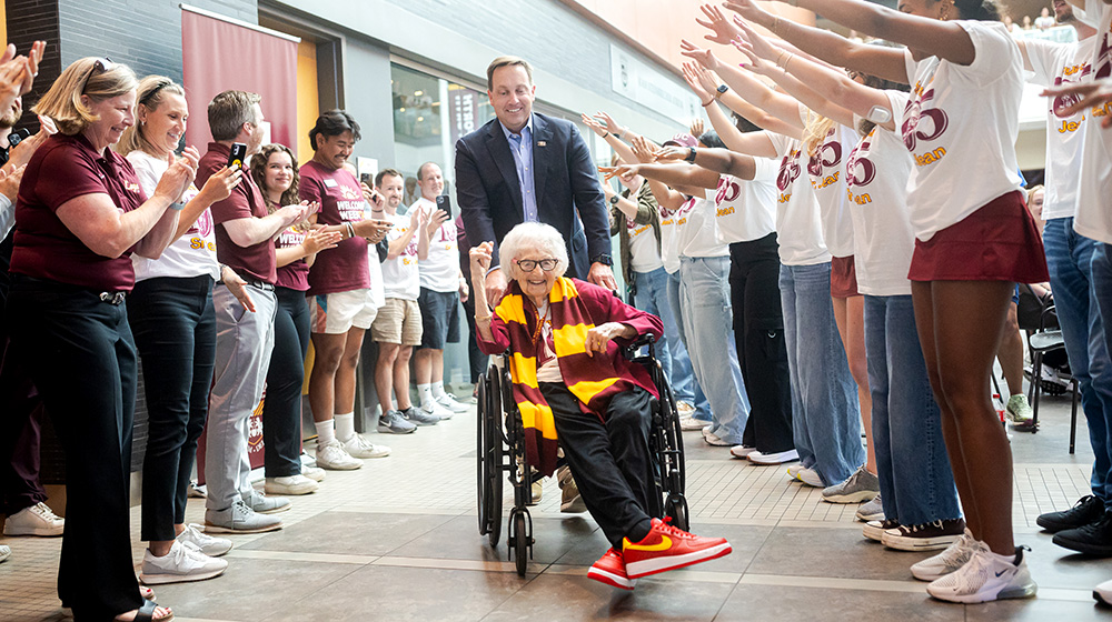 Sister Jean sits in a wheelchair pushed by President Reed.